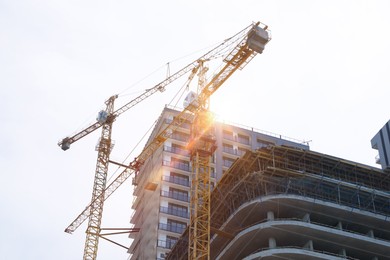 Construction site with tower cranes near unfinished building, low angle view