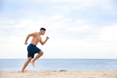 Photo of Muscular man running on beach, space for text