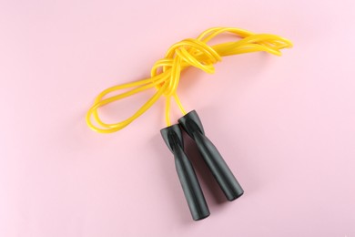 Skipping rope on light pink background, top view. Sports equipment