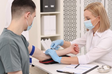 Photo of Doctor taking blood sample from patient with syringe at white table in hospital