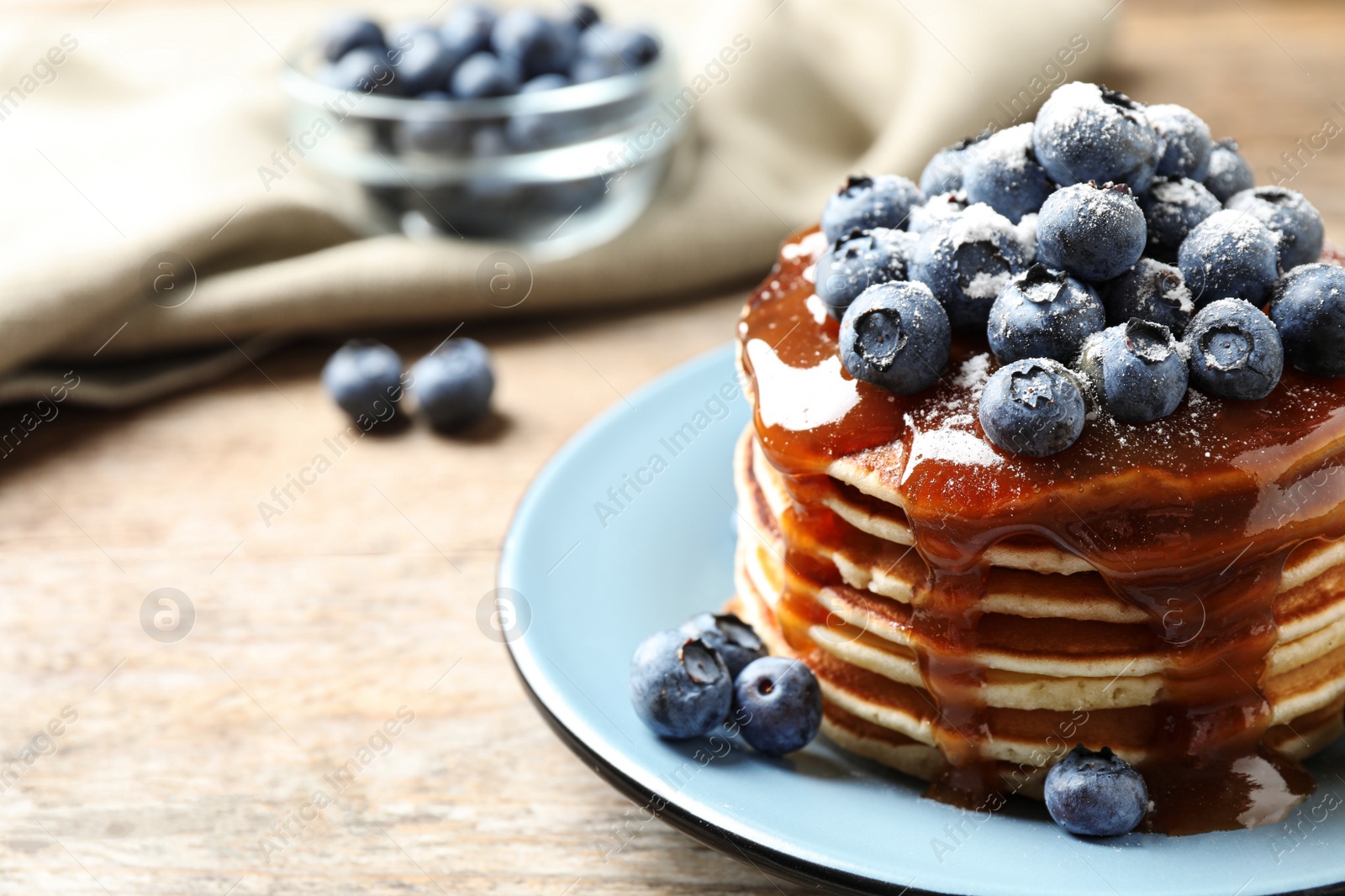 Photo of Delicious pancakes with fresh blueberries and syrup on wooden table, closeup