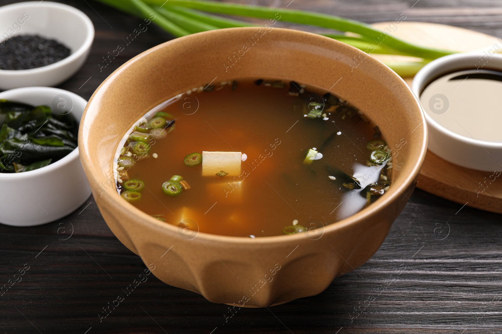 Photo of Bowl of delicious miso soup with tofu on dark wooden table, closeup