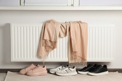 Photo of Heating radiator with scarf and shoes near window in room