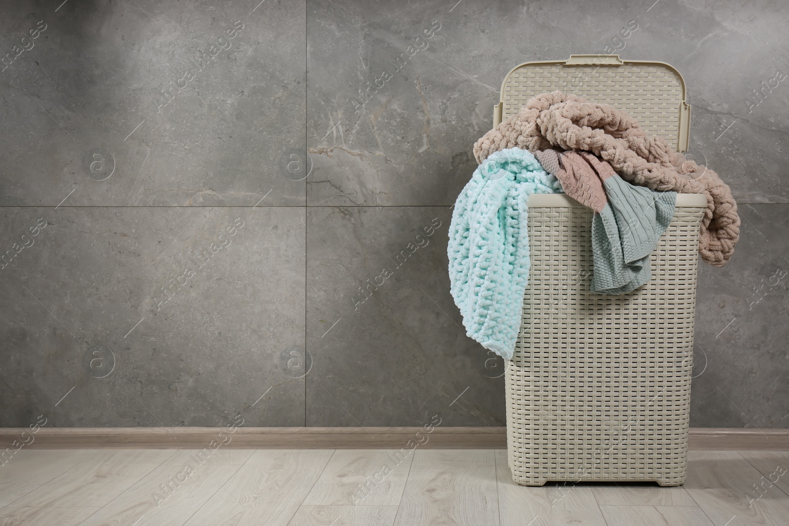 Photo of Laundry basket with clothes near grey wall. Space for text