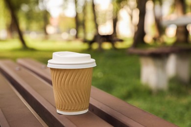 Photo of Paper cup on wooden bench in park, space for text. Coffee to go