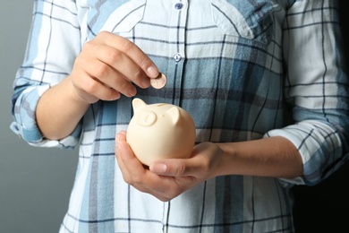 Photo of Young woman putting coin into piggybank on grey background, closeup view