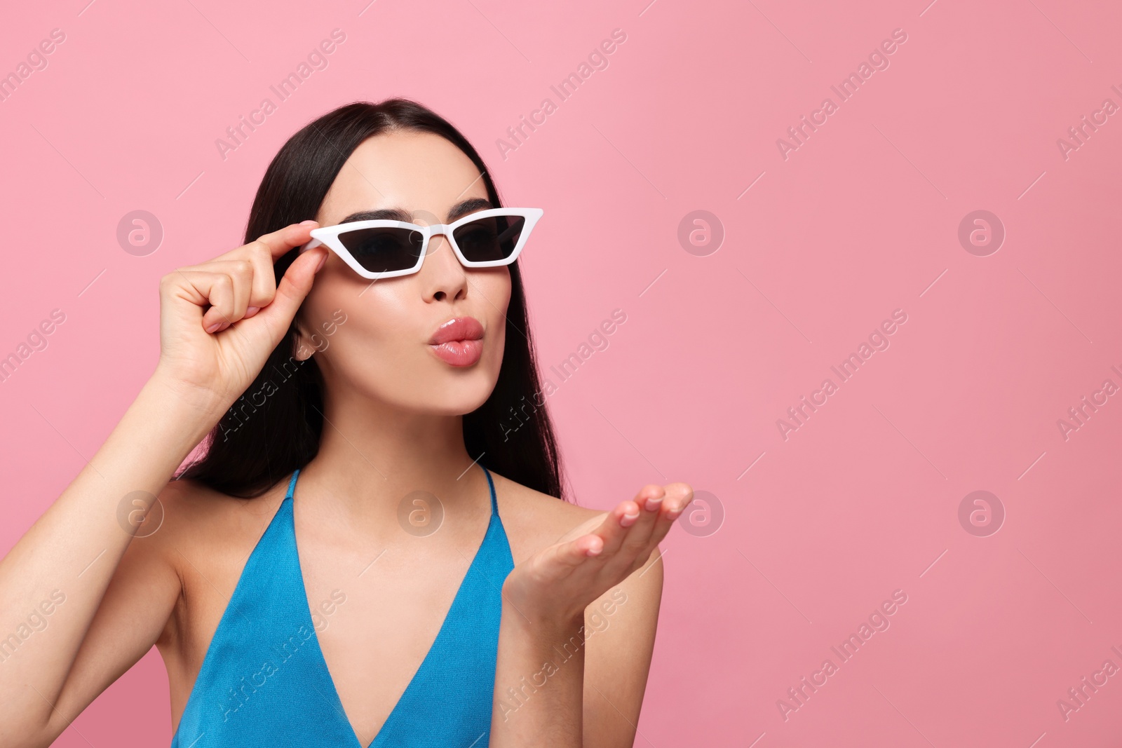 Photo of Beautiful young woman in stylish sunglasses blowing kiss on pink background. Space for text