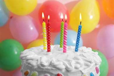 Photo of Delicious cake with cream and burning against balloons, closeup