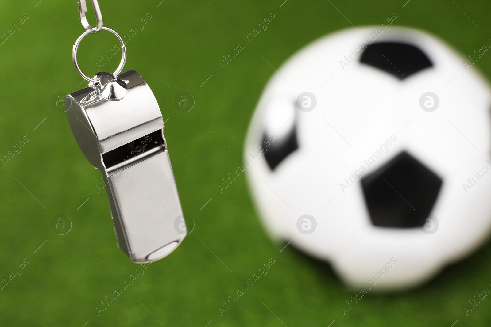 Photo of Football referee equipment. Metal whistle and soccer ball on green grass, closeup with space for text