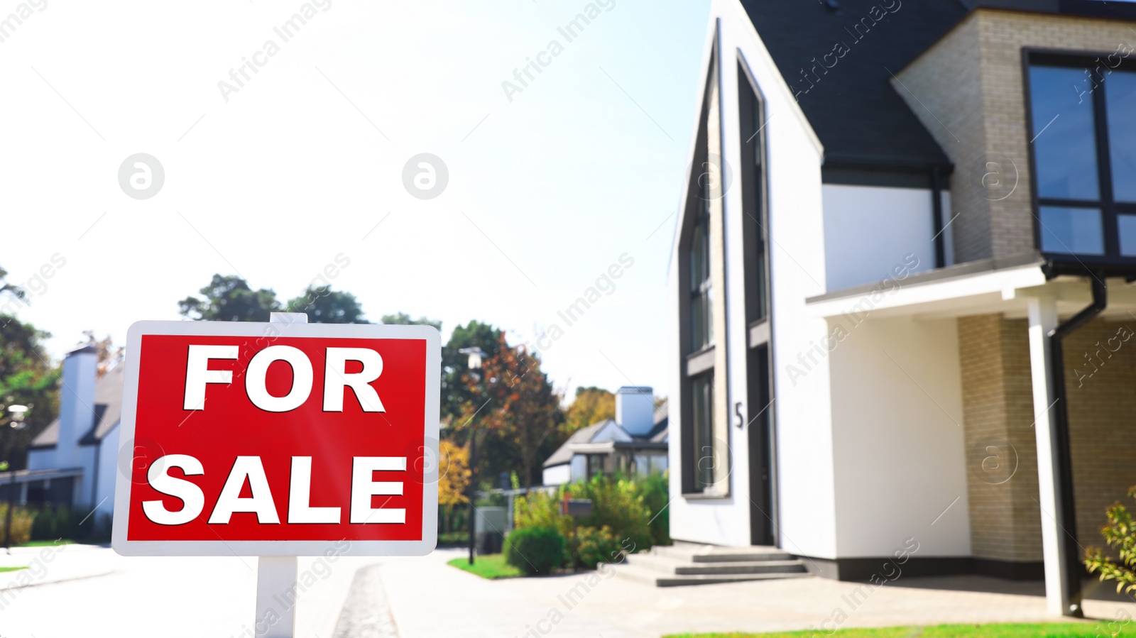 Photo of Red real estate sign near house outdoors on sunny day