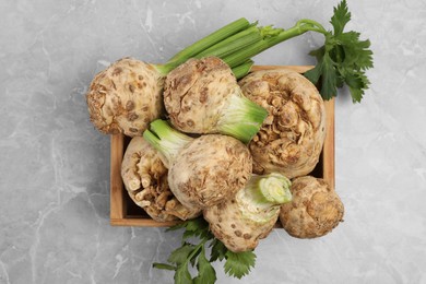Photo of Fresh raw celery roots in wooden crate on light grey table, top view