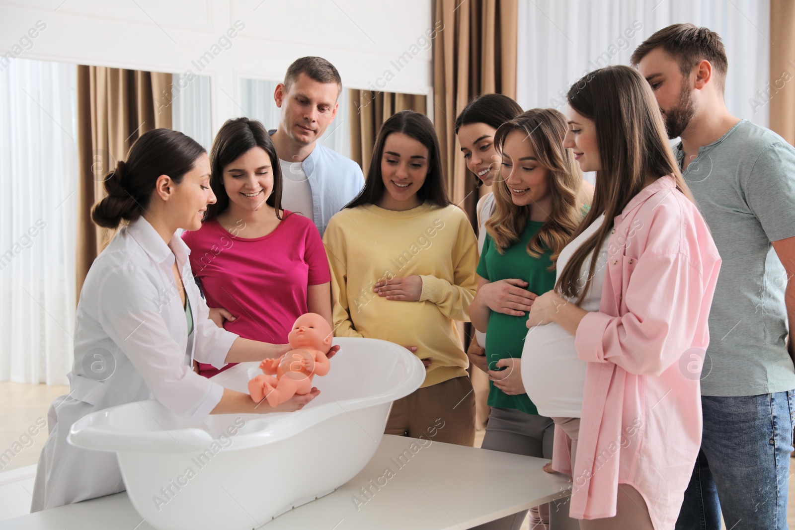 Photo of Pregnant women with men learning how to bathe baby at courses for expectant parents indoors