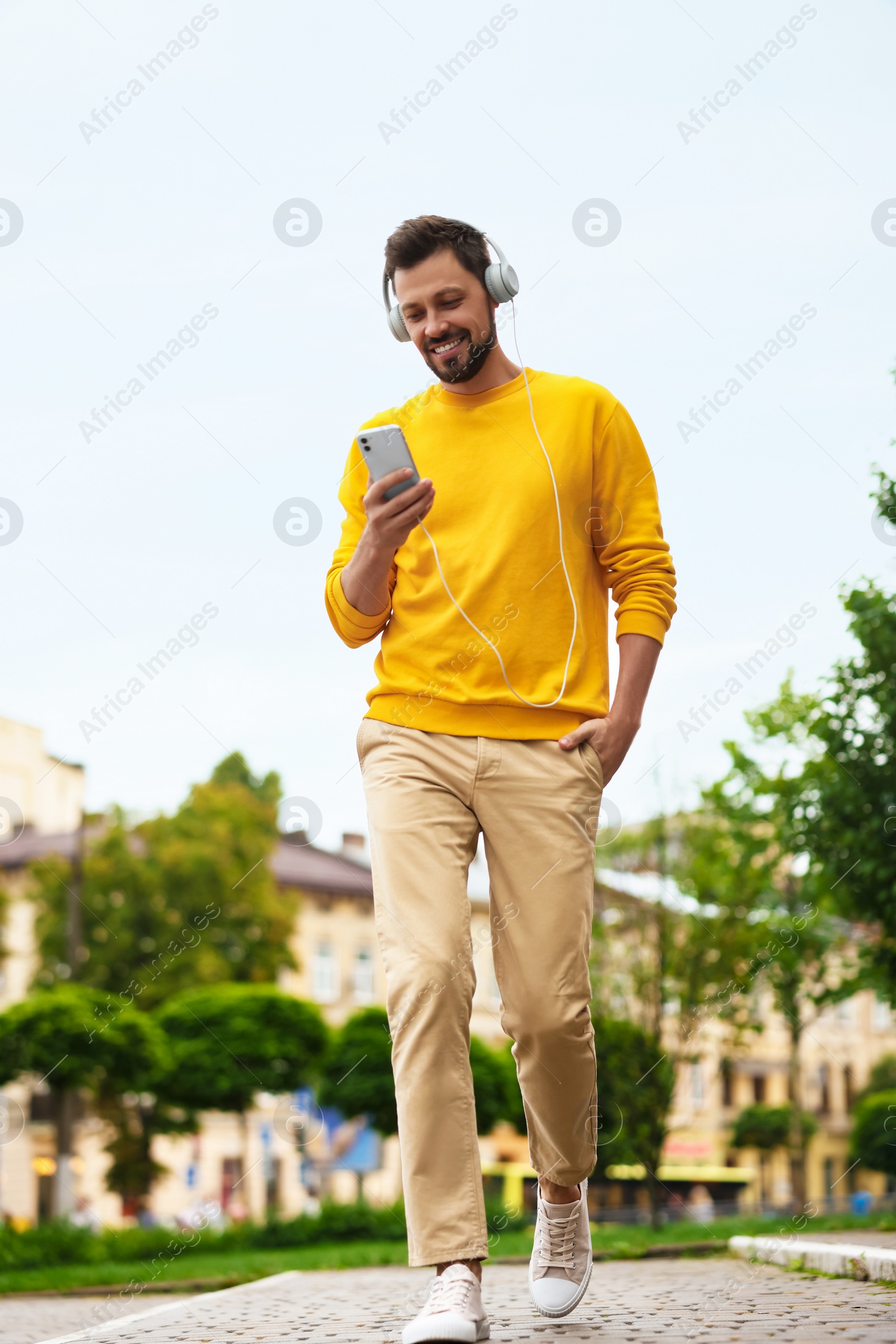 Photo of Handsome man with smartphone and headphones walking on city street