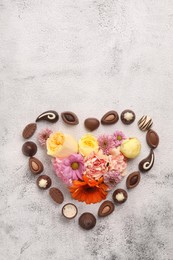 Photo of Heart made with delicious chocolate candies and beautiful flowers on grey table, flat lay. Space for text