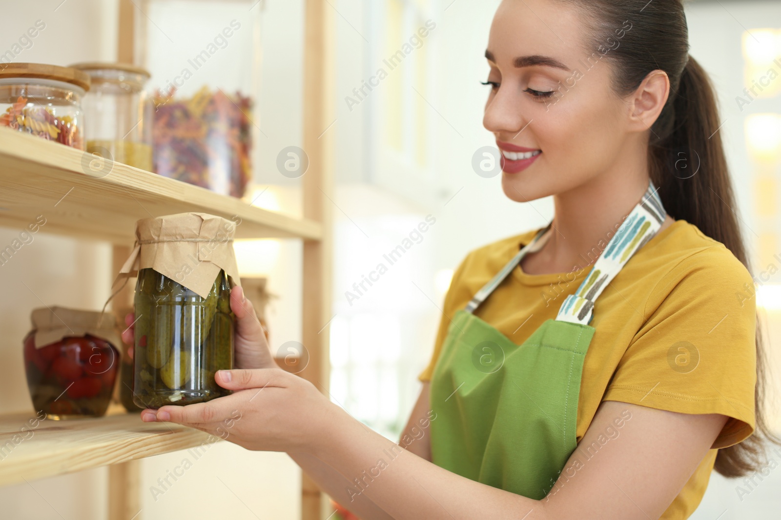Photo of Woman putting jar of pickles on shelf indoors