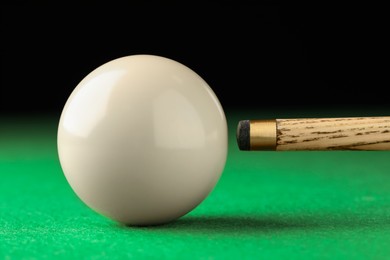 Photo of Classic plain billiard ball and cue on green table, closeup