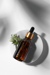 Bottle of cosmetic oil and flower on white background, top view