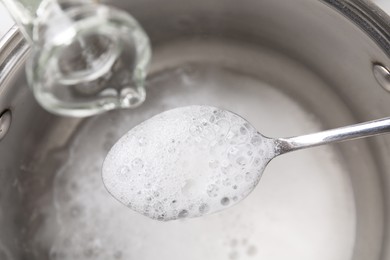 Photo of Pouring vinegar into spoon with baking soda over saucepan, closeup