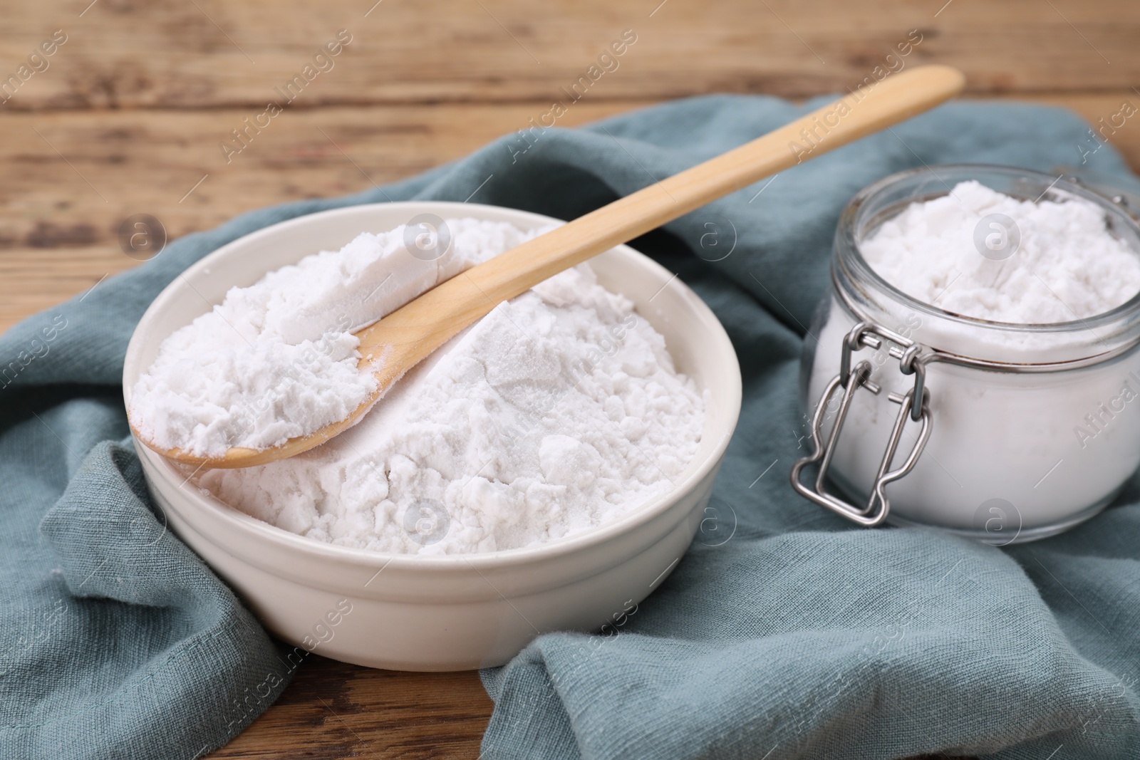 Photo of Bowl, spoon and glass jar of natural starch on wooden table, closeup