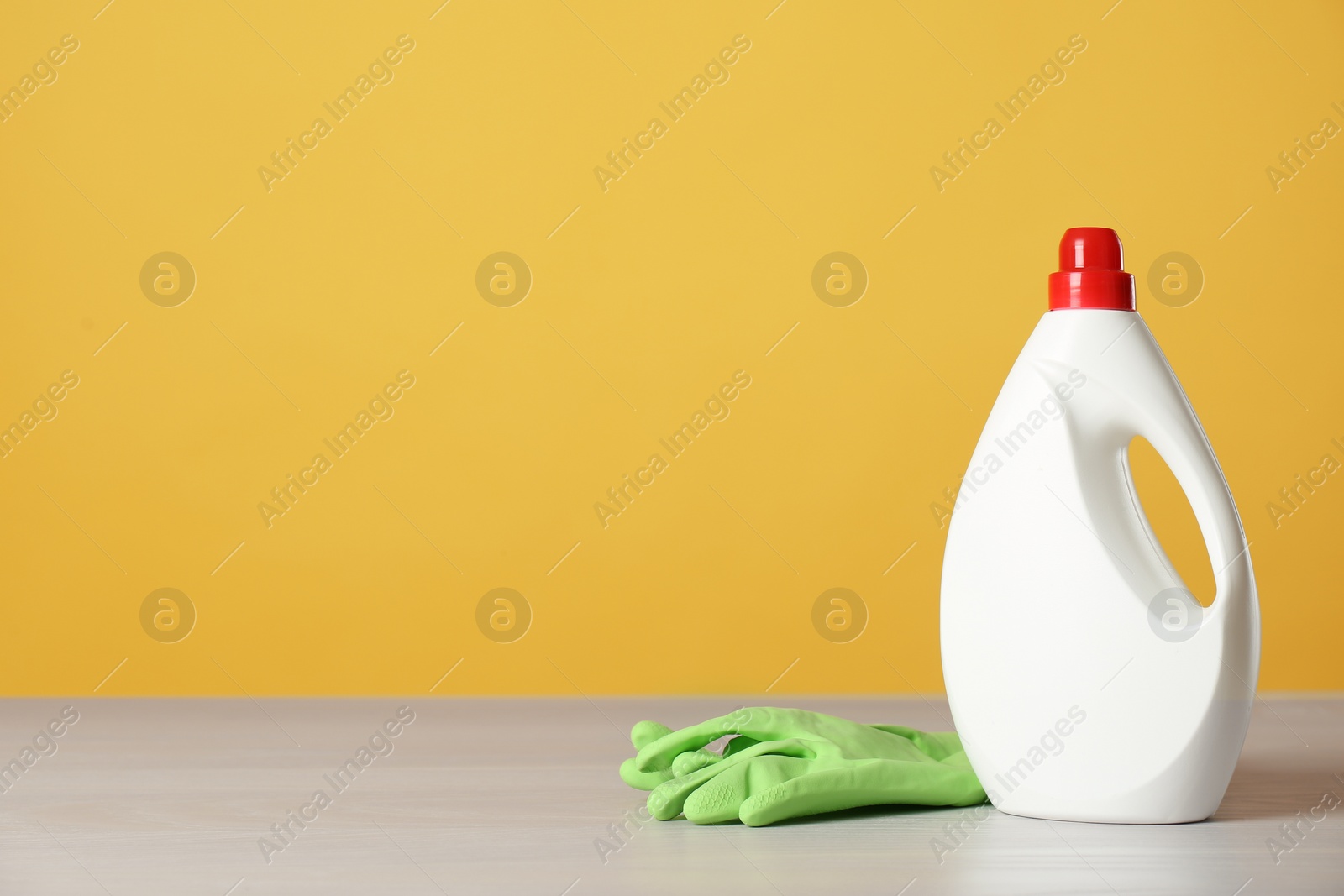 Photo of Bottle of cleaning product and gloves on light table. Space for text