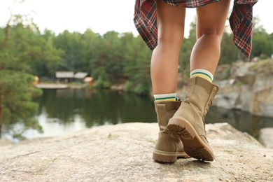 Photo of Young woman in boots on rock, focus on legs. Camping season