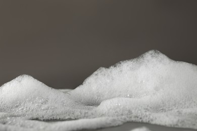 Photo of Fluffy bath foam on grey background, closeup