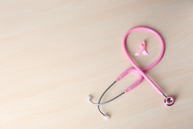 Photo of Pink ribbon with stethoscope on wooden background, space for text. Breast cancer concept