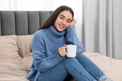 Happy young woman holding white ceramic mug on bed at home