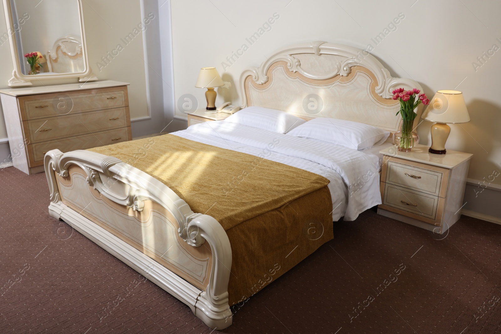 Photo of Stylish bedroom interior with comfortable bed, mirror and beautiful bouquet on bedside table