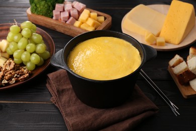 Fondue pot with melted cheese and different products on black wooden table