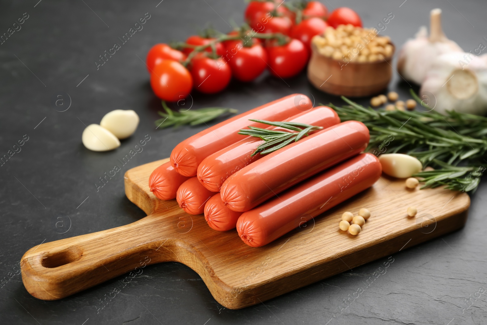 Photo of Fresh raw vegetarian sausages and vegetables on black table