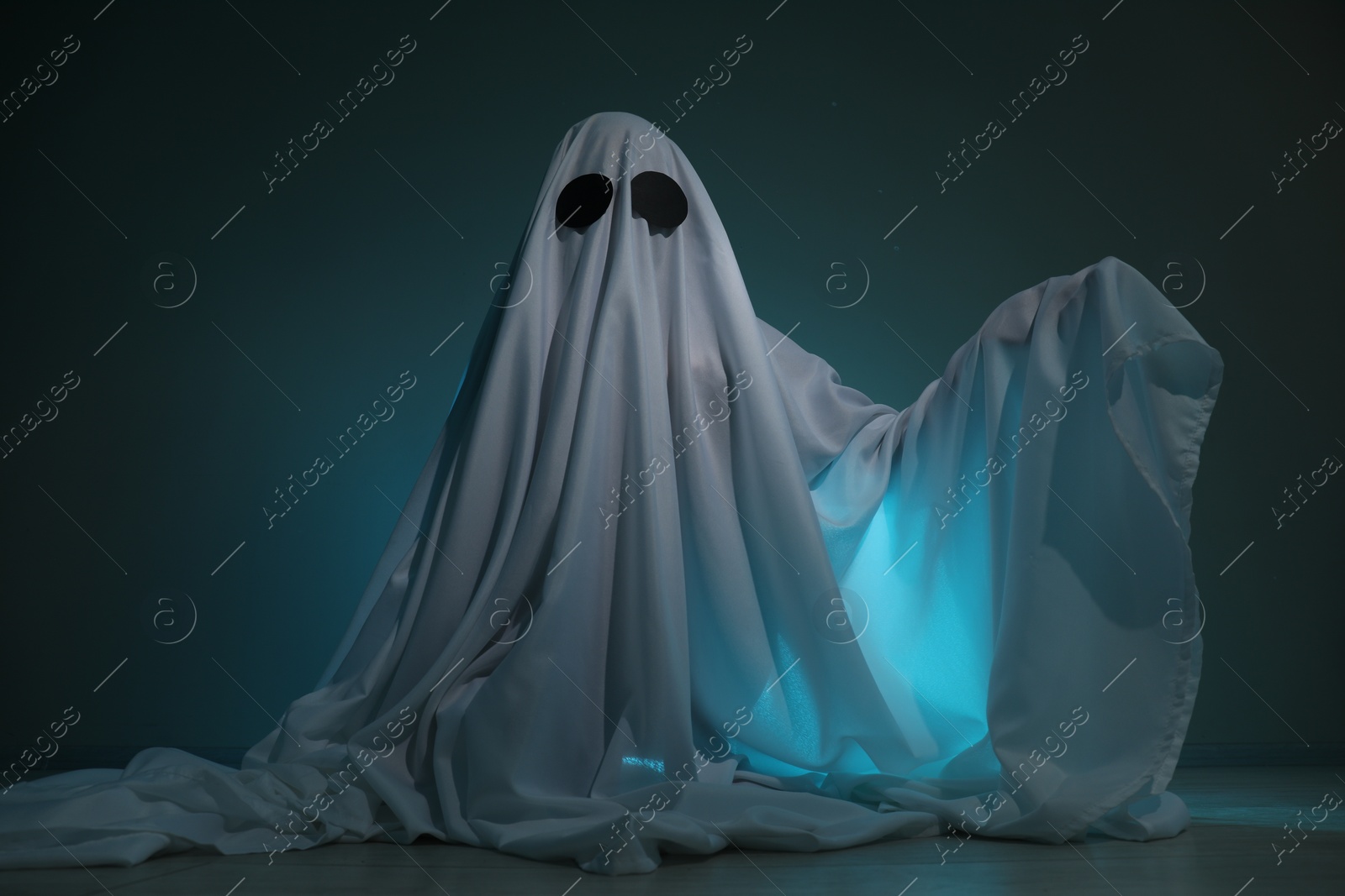 Photo of Creepy ghost. Woman covered with sheet on dark teal background