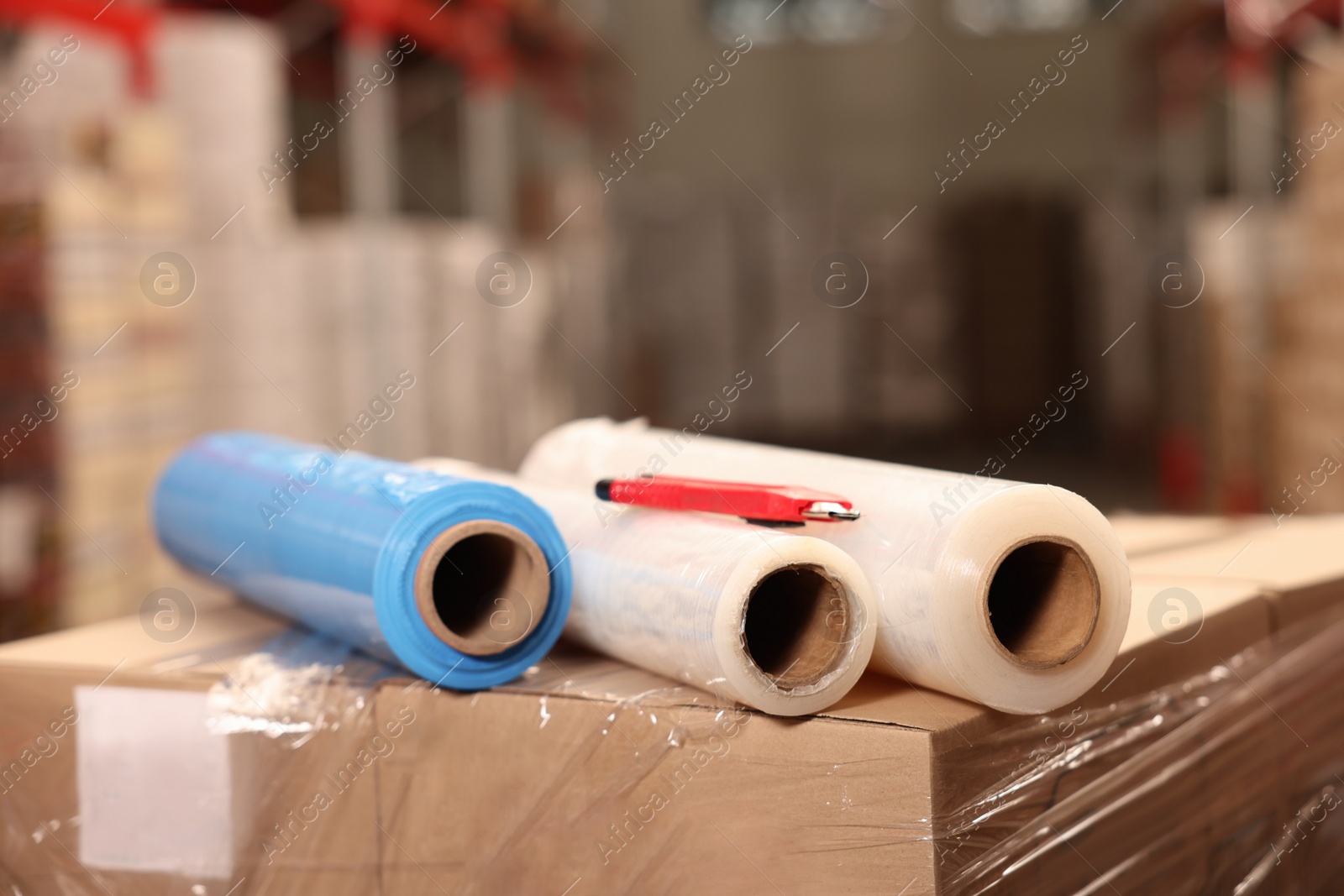 Photo of Rolls of different stretch wraps and utility knife on boxes in warehouse