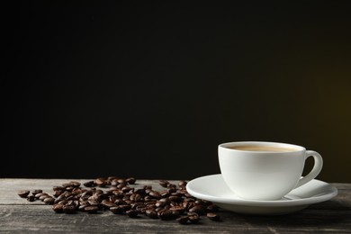 Cup of hot aromatic coffee and roasted beans on wooden table against dark background, space for text