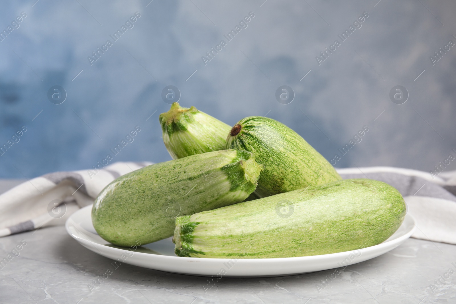 Photo of Plate with fresh ripe zucchini on grey table against blue background