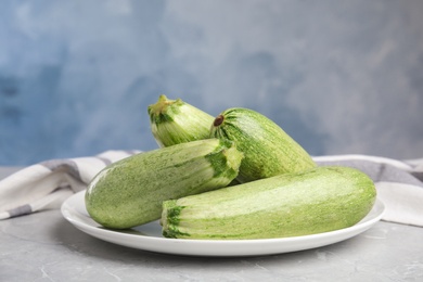 Photo of Plate with fresh ripe zucchini on grey table against blue background