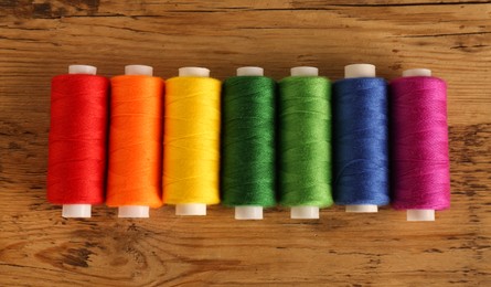 Photo of Different colorful sewing threads on wooden background, flat lay