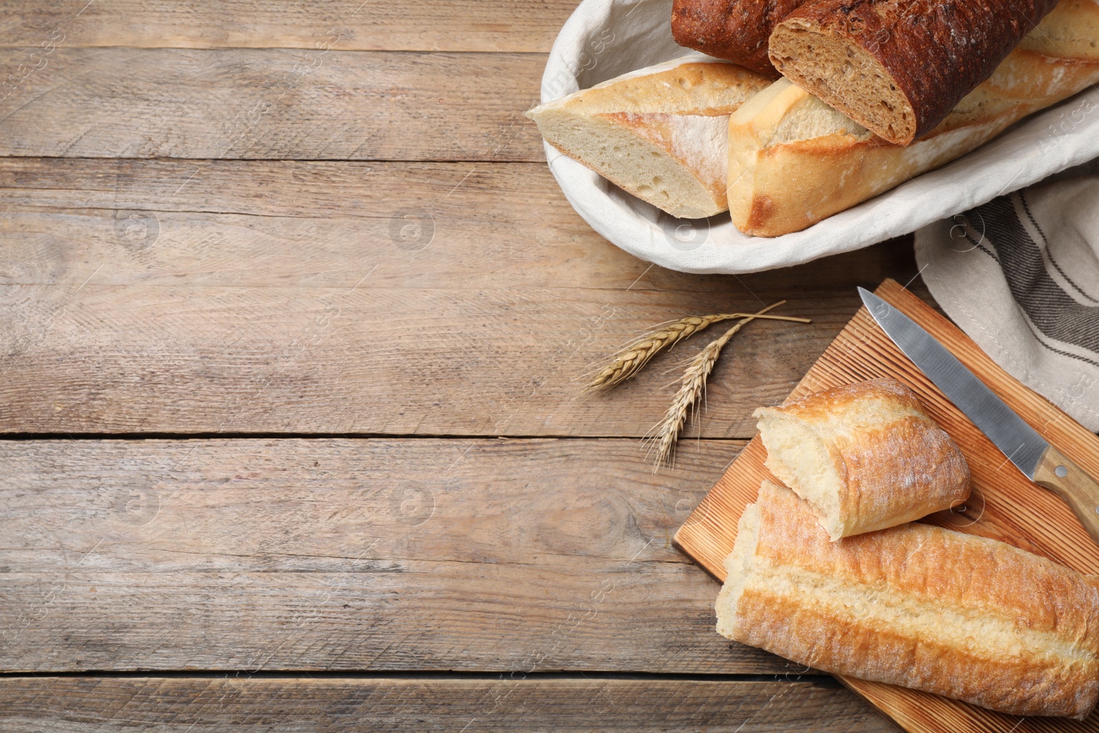 Photo of Different tasty baguettes, knife and spikelets on wooden table, flat lay. Space for text