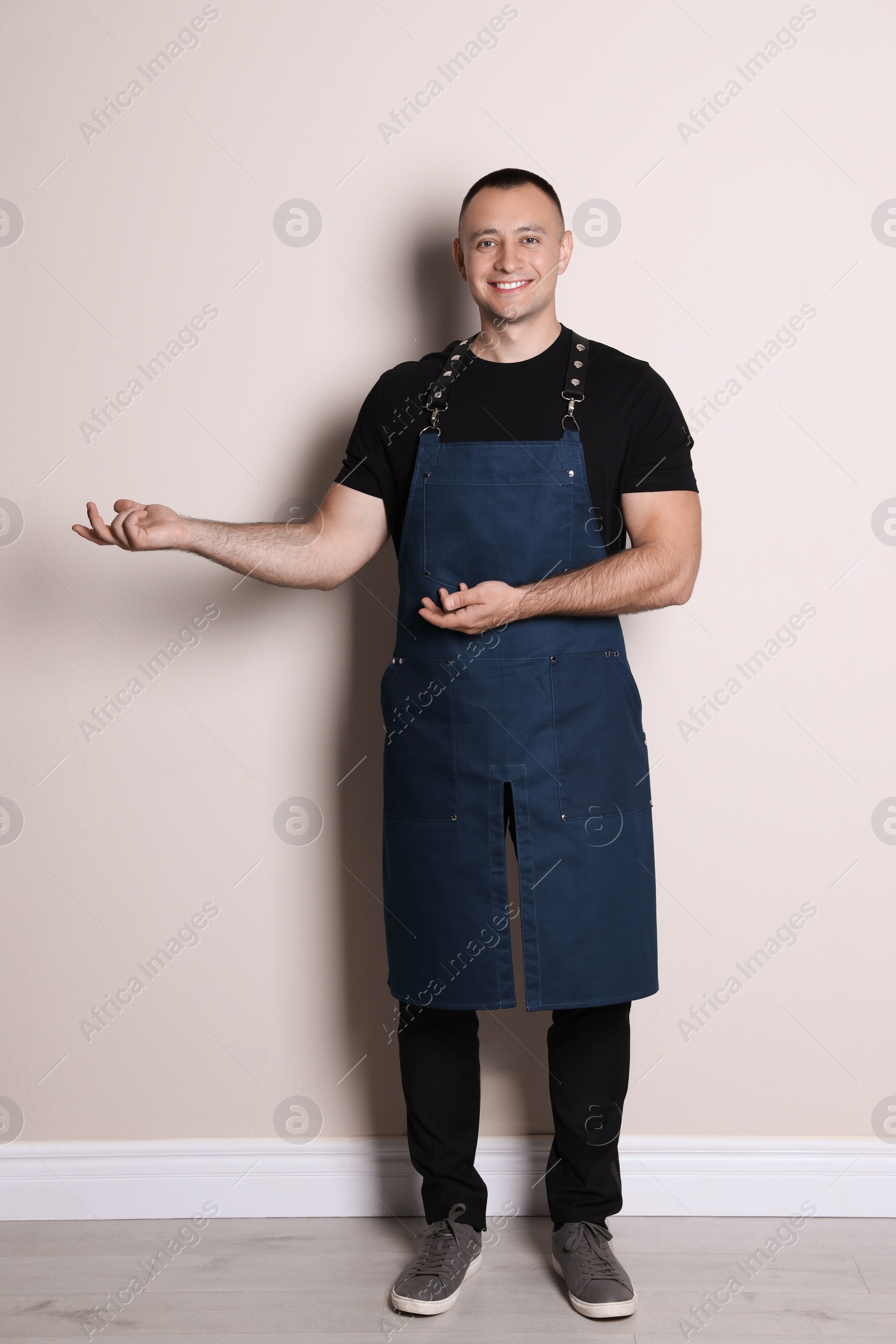 Photo of Full length portrait of happy young waiter in uniform near light wall indoors
