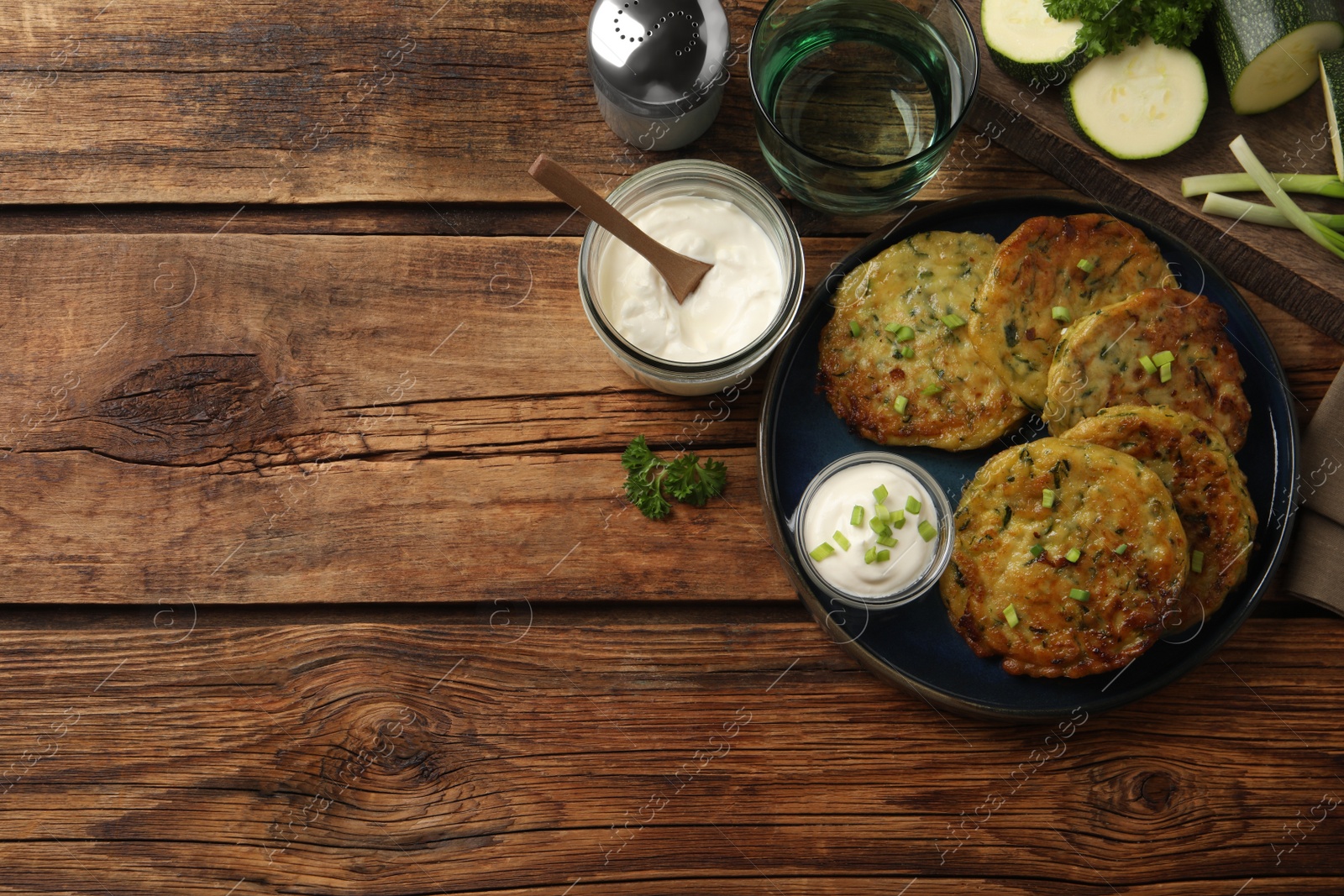 Photo of Delicious zucchini fritters with sour cream served on wooden table, flat lay. Space for text