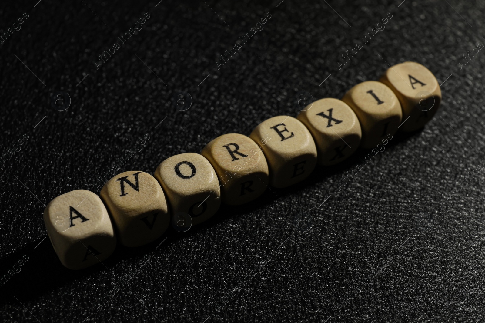 Photo of Word Anorexia made of wooden cubes on black background, closeup