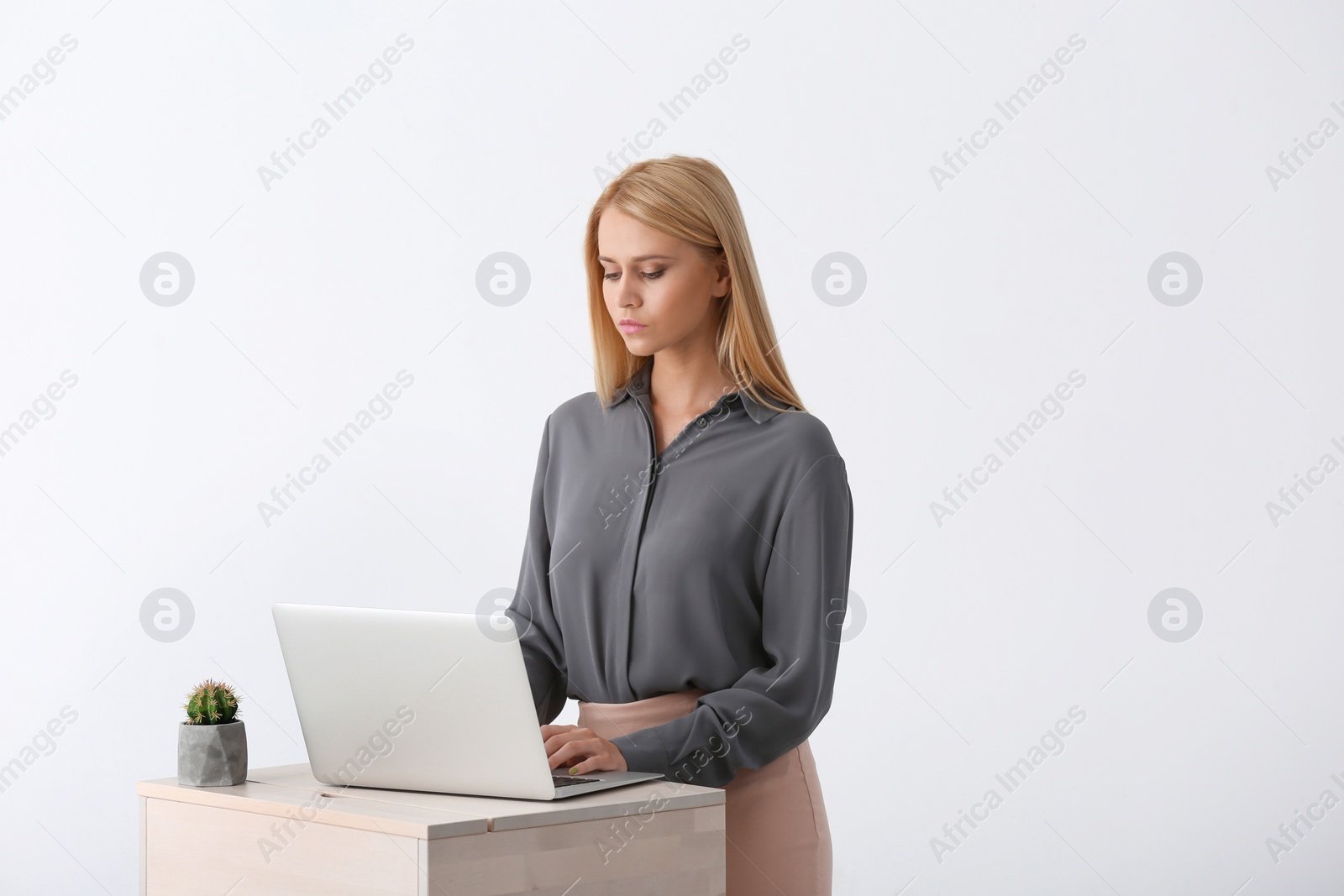 Photo of Young woman using laptop at stand up workplace against white wall