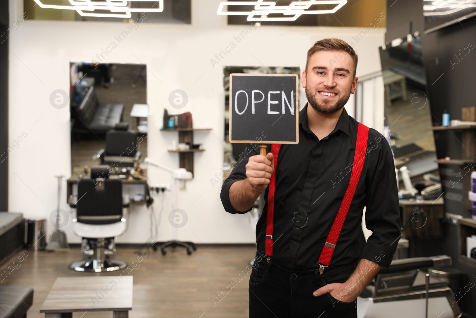 Photo of Young business owner holding OPEN sign in his barber shop