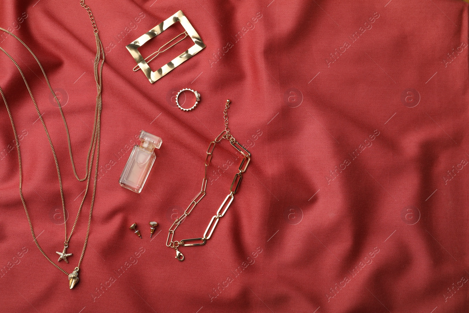 Photo of Stylish golden bijouterie and perfume on red fabric, flat lay. Space for text