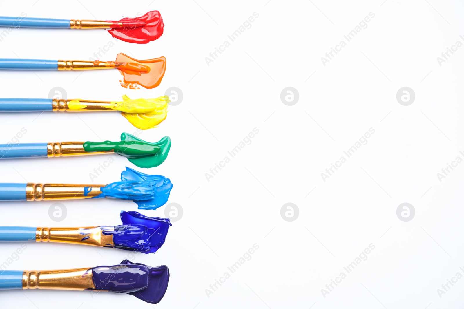 Photo of Set of brushes with different paints on white background, flat lay. Rainbow colors