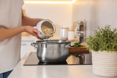 Photo of Woman adding noodles into pot with soup in kitchen, closeup