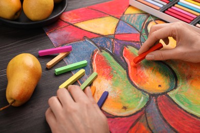 Photo of Woman drawing pears on paper with soft pastels at wooden table, closeup