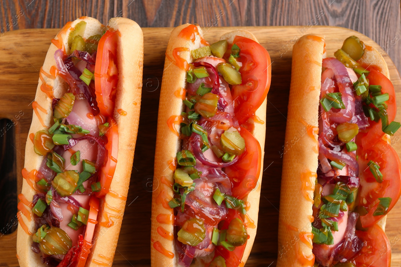 Photo of Tasty hot dogs with green onion, tomato, pickles and sauce on wooden table, top view