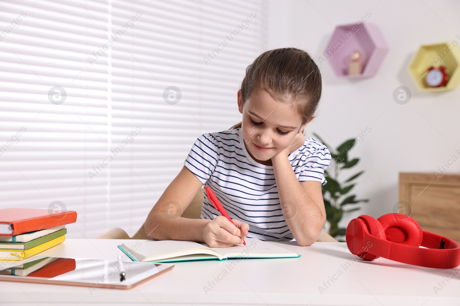 Photo of E-learning. Cute girl taking notes while studying online at table indoors