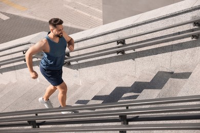 Smiling man running up stairs outdoors on sunny day. Space for text